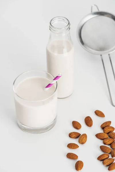 Organic almond milk in bottle and glass with straw near scattered almonds and sieve — Stock Photo