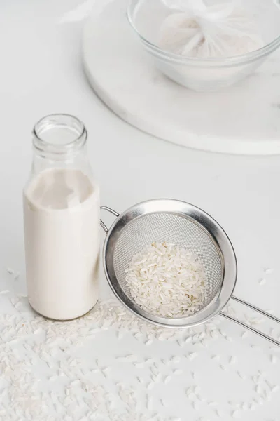 Selective focus of rice milk in bottle near rice and sieve with rice in cheesecloth on background — Stock Photo