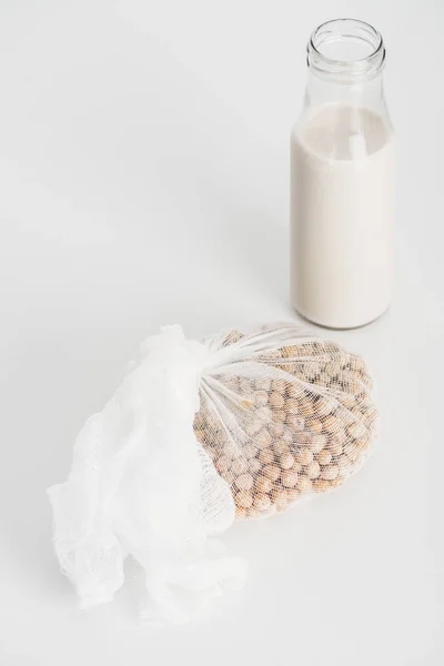 Chickpea in white cheesecloth near bottle with vegan chickpea milk on grey background — Stock Photo