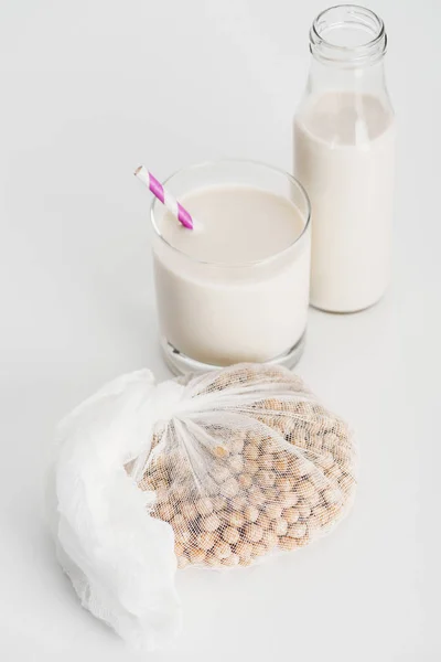 Kichererbse in weißem Käsetuch neben Flasche und Glas mit veganer Kichererbsenmilch auf grauem Hintergrund — Stockfoto