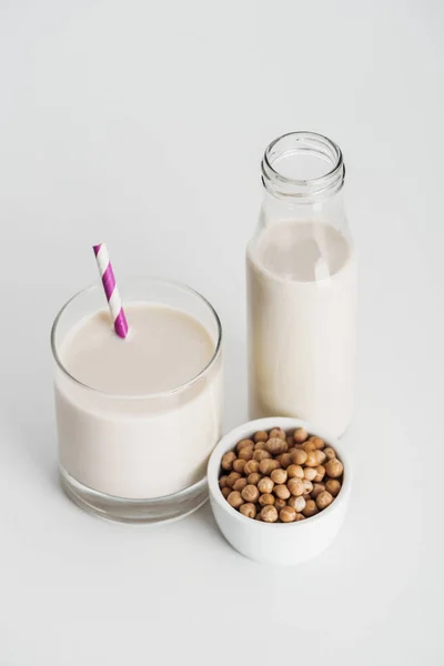 Chickpea in bowl near bottle and glass with vegan chickpea milk on grey background — Stock Photo