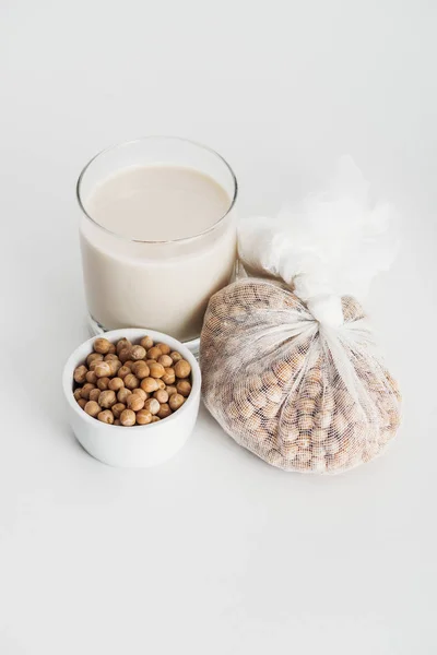 Chickpea in bowl and cheesecloth near vegan chickpea milk in glass on grey background — Stock Photo