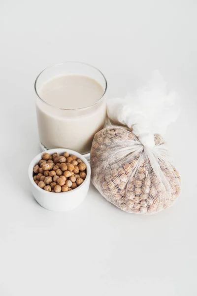 Garbanzo en tazón y mantel de queso cerca de la leche de garbanzo vegano en vaso sobre fondo gris - foto de stock