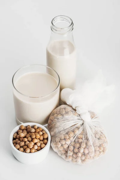 Chickpea in bowl and cheesecloth near vegan chickpea milk in glass and bottle on grey background — Stock Photo