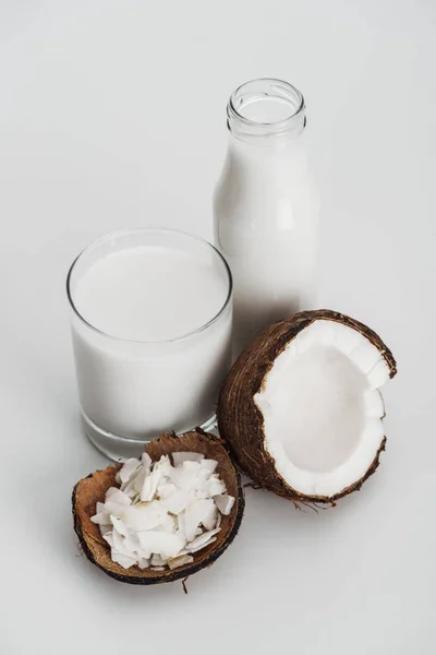 Leite de coco vegan orgânico em vidro e garrafa perto da metade de coco e batatas fritas de coco em fundo cinza — Fotografia de Stock