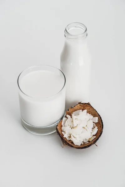 Organic vegan coconut milk in glass near coconut chips on grey background — Stock Photo