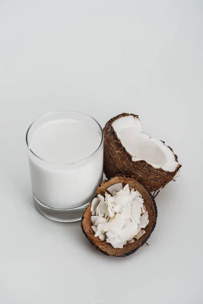 Bio-vegane Kokosmilch im Glas in der Nähe der Kokosnusshälfte und Chips auf grauem Hintergrund — Stockfoto