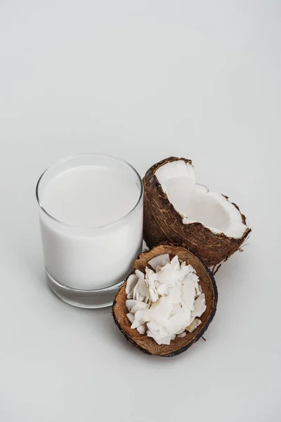 Leite de coco vegan orgânico em vidro perto da metade de coco e batatas fritas em fundo cinza — Fotografia de Stock