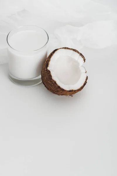 Organic vegan coconut milk in glass near coconut half and cheesecloth on grey background — Stock Photo