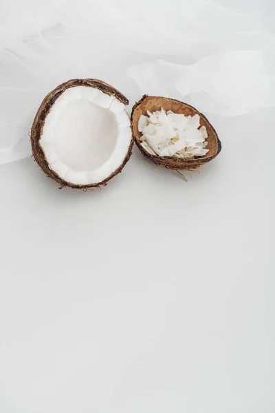 Fresh coconut half and chips near cheesecloth on grey background — Stock Photo