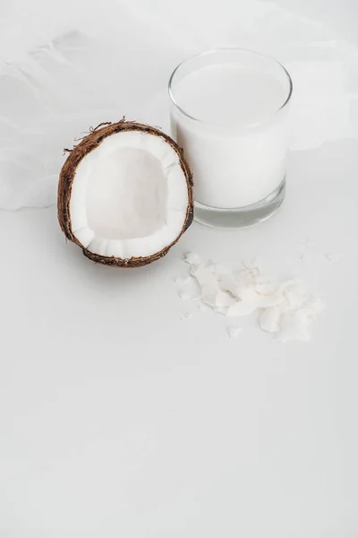 Lait de coco végétalien biologique en verre près de la moitié de noix de coco, copeaux et étamine sur fond gris — Photo de stock