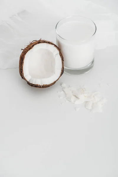 Leche de coco vegana orgánica en vidrio cerca de la mitad de coco, patatas fritas y mantel de queso sobre fondo gris - foto de stock