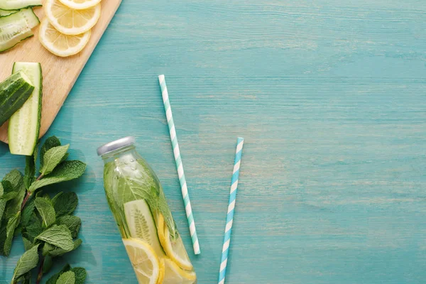 Vue du dessus de boisson de désintoxication en bouteille près de tranches de citron et de concombre, menthe et pailles — Photo de stock