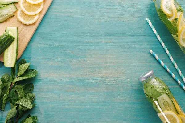 Vista superior de la bebida desintoxicante en botellas cerca de rodajas de limón y pepino, menta y pajitas - foto de stock