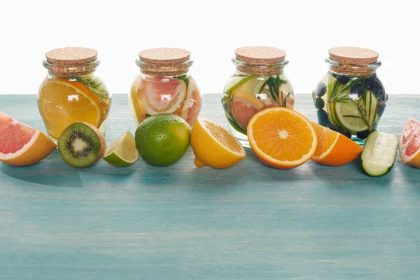 Bebidas desintoxicação em frascos com frutas, legumes, ervas, bagas e vegetação perto de ingredientes na superfície azul de madeira isolada em branco — Fotografia de Stock