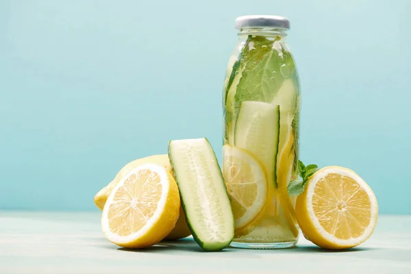 Bebida desintoxicante en botella cerca de limones, menta y pepino aislado en azul - foto de stock