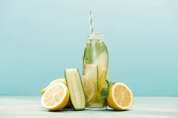 Boisson de désintoxication en bouteille avec de la paille près de citrons, menthe et concombre isolé sur bleu — Photo de stock