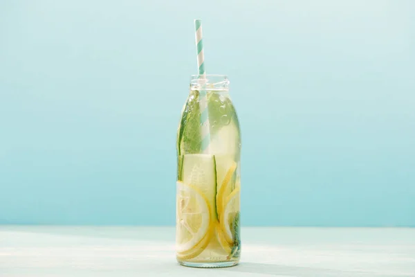 Bebida desintoxicante en botella con paja, limones, menta y pepinos aislados en azul - foto de stock