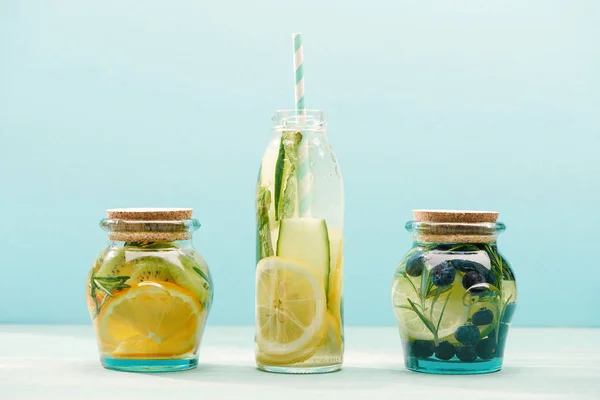 Bebidas desintoxicantes en botella abierta con paja y frascos aislados en azul - foto de stock