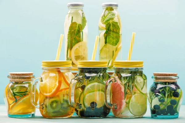 Bebidas desintoxicantes orgánicas con bayas, frutas y verduras en frascos y botellas con pajitas aisladas en azul - foto de stock