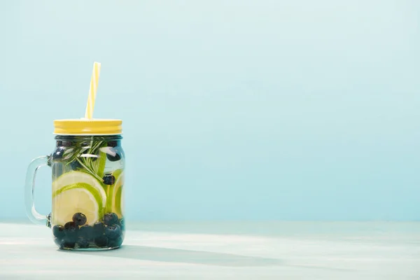 Boisson de désintoxication dans un bocal avec romarin, bleuets, citrons verts et paille isolé sur bleu — Photo de stock