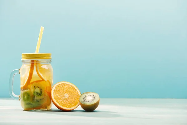 Detox drink in jar with straw near orange and kiwi isolated on blue — Stock Photo