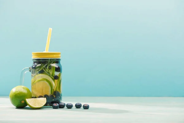 Свежий детоксикационный напиток в банке с соломой рядом с черникой и лаймами, изолированными на голубом — стоковое фото