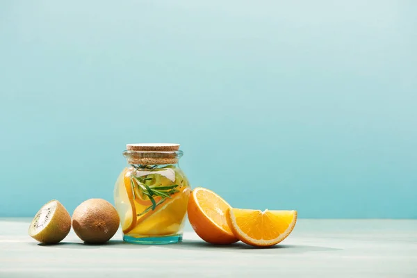 Boisson de désintoxication aux fruits bio dans un bocal avec romarin près des oranges et kiwi isolé sur bleu — Photo de stock