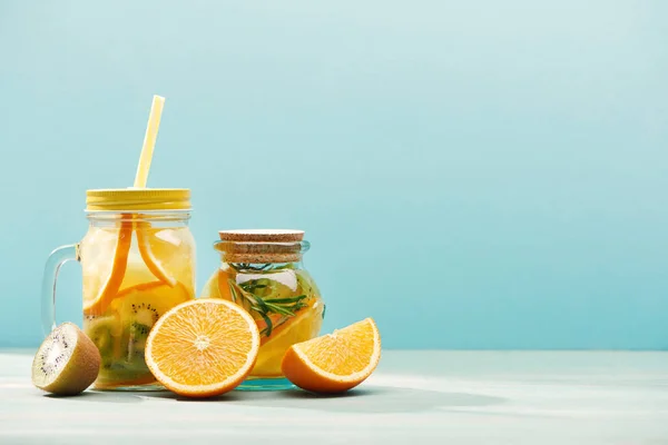 Organic fruit detox drinks in jars near oranges and kiwi isolated on blue — Stock Photo