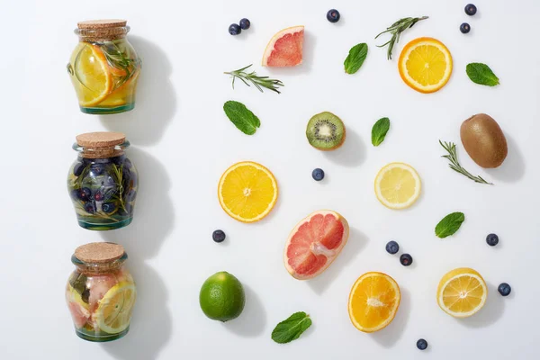 Vista dall'alto di bevande disintossicanti in barattoli vicino a fette di frutta, mirtilli, menta e rosmarino — Foto stock