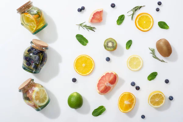 Top view of detox drinks in jars near fruit slices, blueberries and herbs — Stock Photo