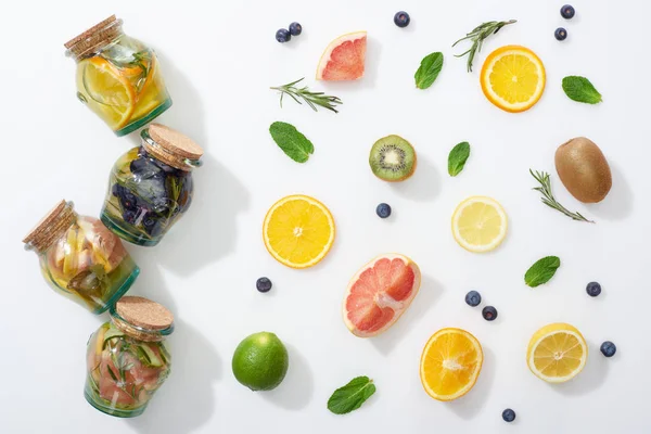 Top view of detox drinks in jars near fruit slices, berries, mint and rosemary — Stock Photo