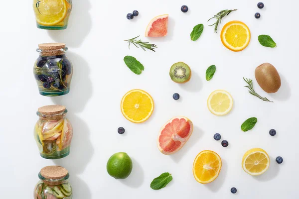 Vista dall'alto di bevande disintossicanti in barattoli vicino a fette di frutta, bacche ed erbe — Foto stock