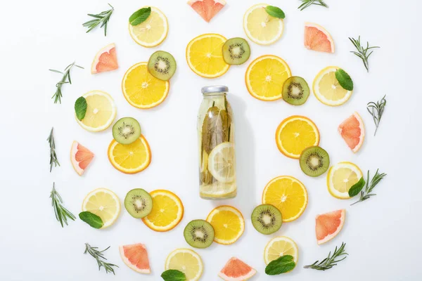 Posa piatta con kiwi affettato, arance, limoni, pompelmi, menta, rosmarino e bevanda disintossicante in bottiglia su fondo grigio — Foto stock