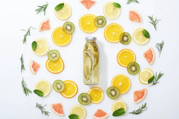 Acostado plano con kiwi en rodajas, naranjas, limones, pomelos, menta, romero y bebida de desintoxicación en botella sobre fondo gris - foto de stock