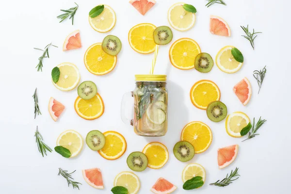 Acostado plano con kiwi en rodajas, naranjas, limones, pomelos, menta, romero y bebida de desintoxicación en frasco sobre fondo gris - foto de stock