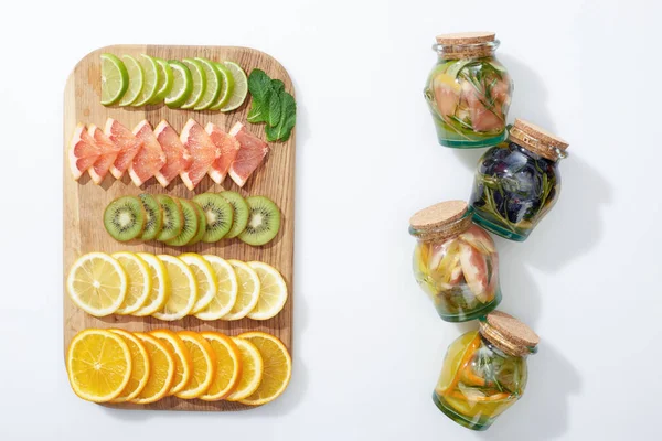 Top view of detox drinks in jars near fruit slices on wooden chopping board — Stock Photo