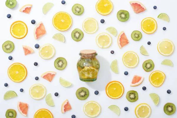 Vista superior da bebida desintoxicação natural em frasco entre frutas fatiadas e mirtilos no fundo branco — Fotografia de Stock