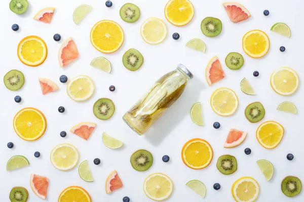 Vista superior da bebida de desintoxicação em garrafa entre frutas fatiadas e mirtilos no fundo branco — Fotografia de Stock