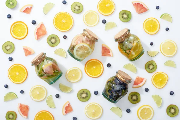 Vista dall'alto di bevande disintossicanti in barattoli tra frutta fresca affettata e mirtilli su sfondo bianco — Foto stock