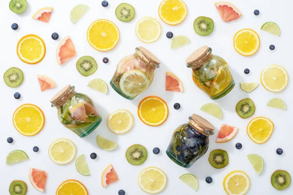 Top view of detox drinks in jars among sliced fresh fruits and blueberries on white background — Stock Photo