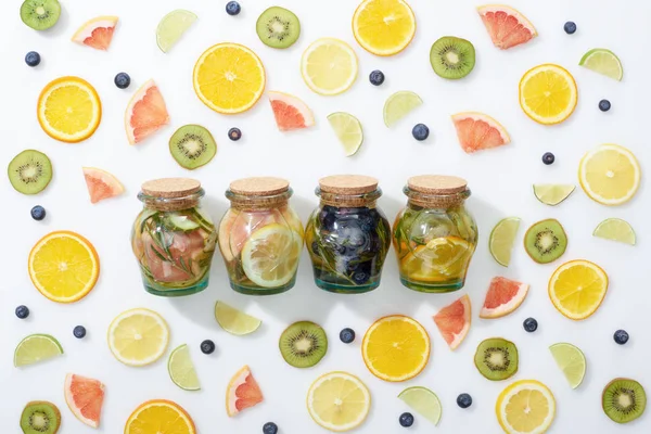 Top view of detox drinks in jars among sliced fruits and blueberries on white background — Stock Photo