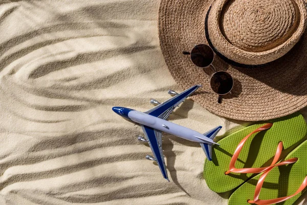 Вид зверху іграшкової площини, солом'яний капелюх, фліп-флоп і сонцезахисні окуляри на хвилястому піску з копіювальним простором — стокове фото