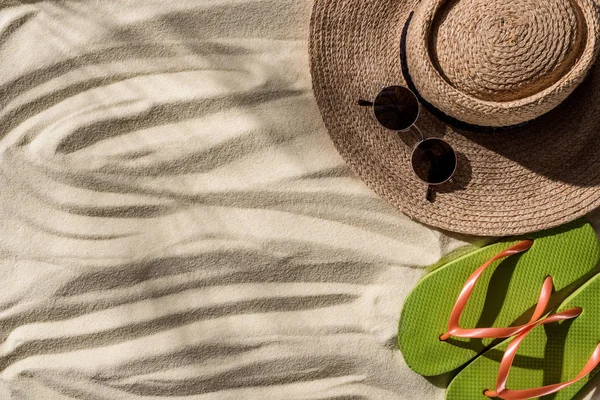 Vista superior de chapéu de palha, chinelos e óculos de sol em areia ondulada com espaço de cópia — Fotografia de Stock