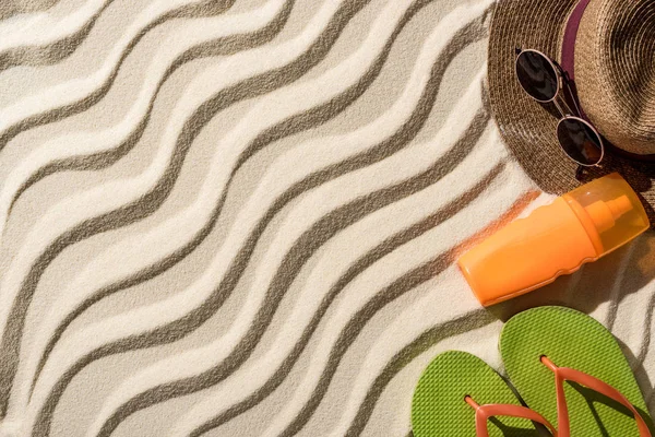 Vista superior de sombrero de paja, chanclas, protector solar y gafas de sol en arena ondulada con espacio para copiar - foto de stock