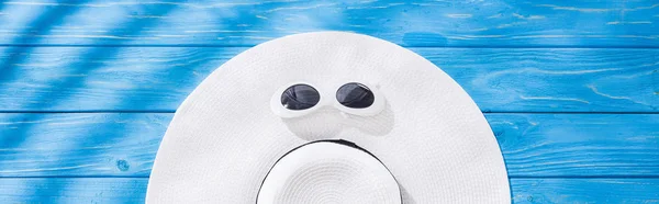 Plano panorámico de sombrero floppy blanco con cinta negra y gafas de sol sobre fondo de madera azul - foto de stock