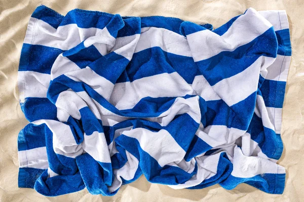 Вид сверху на измятое сине-белое полосатое пляжное полотенце на песке — стоковое фото