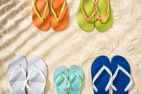 Draufsicht auf weiße, grüne, orangefarbene, türkisfarbene und blaue Flip Flops auf Sand mit Schatten — Stockfoto