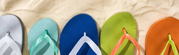 Panoramic shot of white, turquoise, green and blue flip flops on sand — Stock Photo
