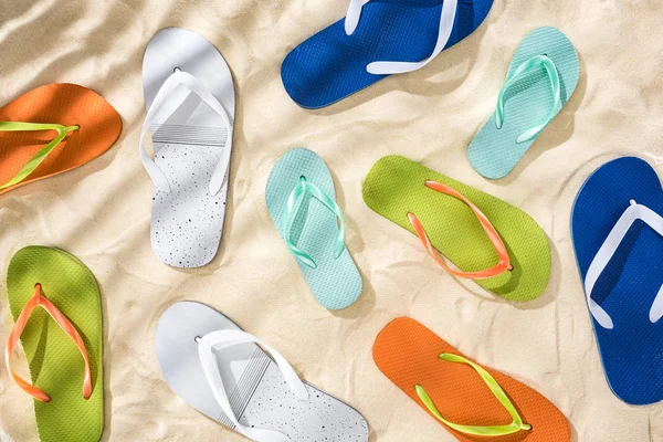 Top view of scattered white, turquoise, green and blue flip flops on sand with shadows — Stock Photo